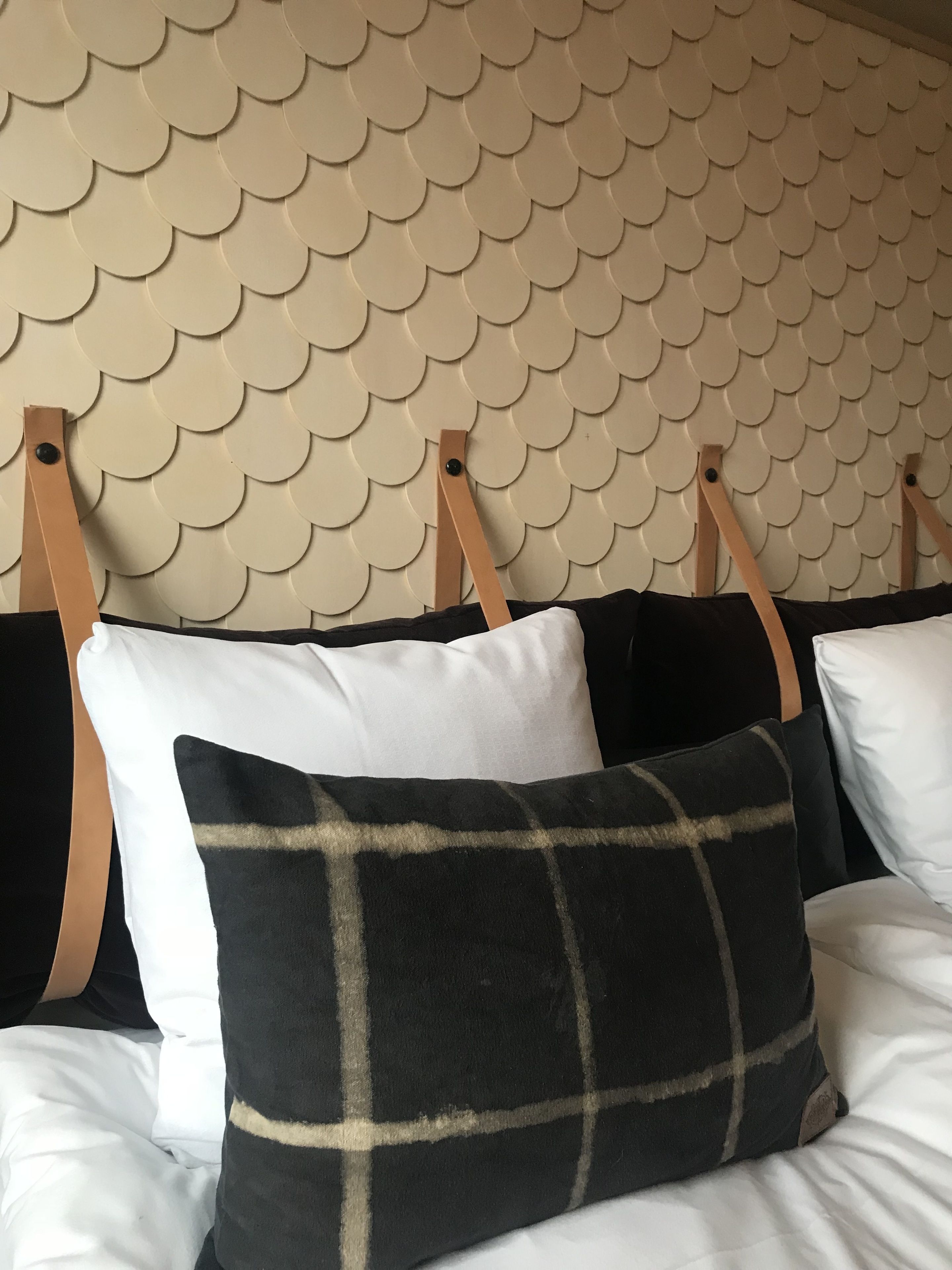 Una cama con cabecera de diseño festoneado, acompañada de almohadas en blanco y negro.