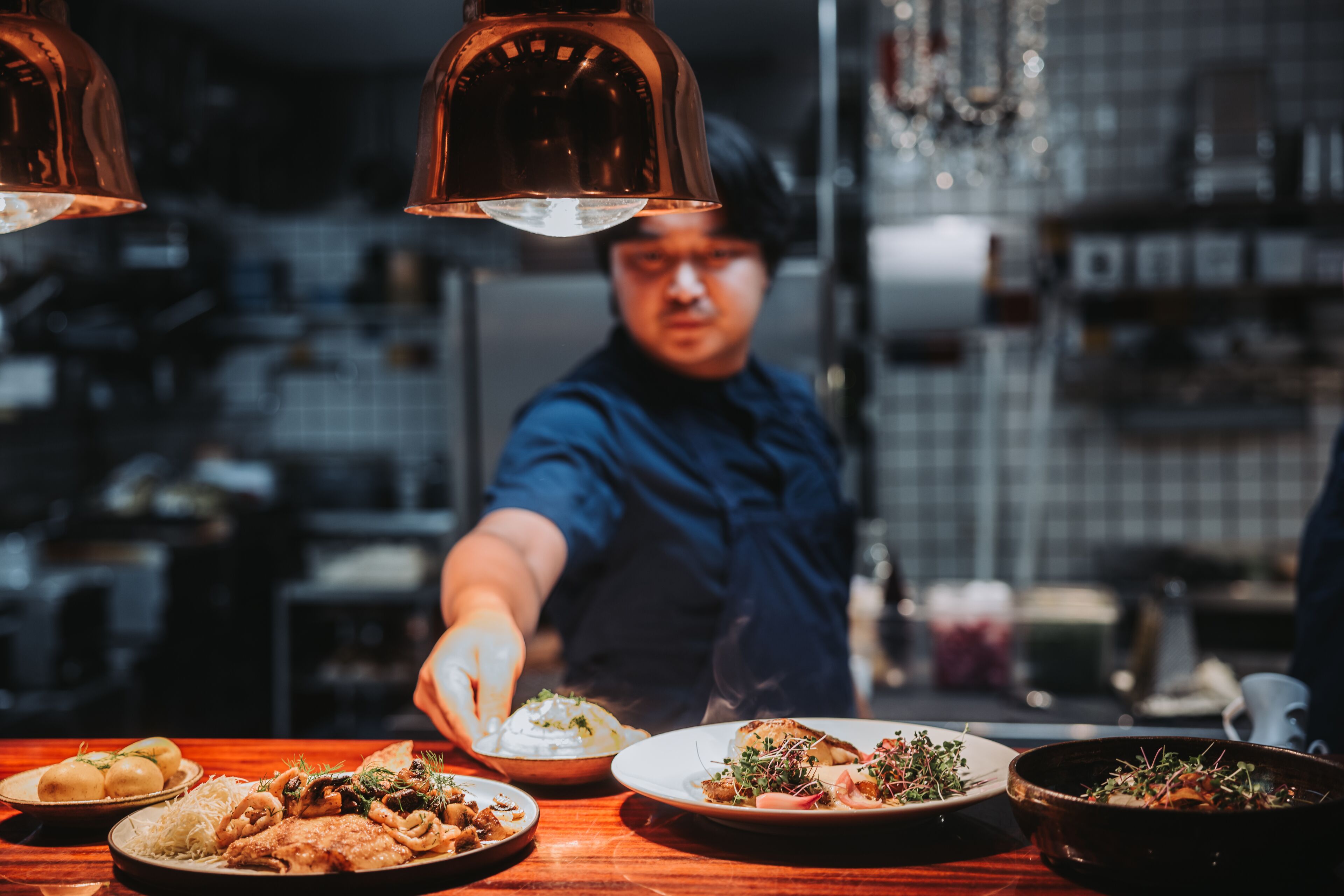 Een kok serveert eten in een keuken met diverse gerechten op het aanrecht.