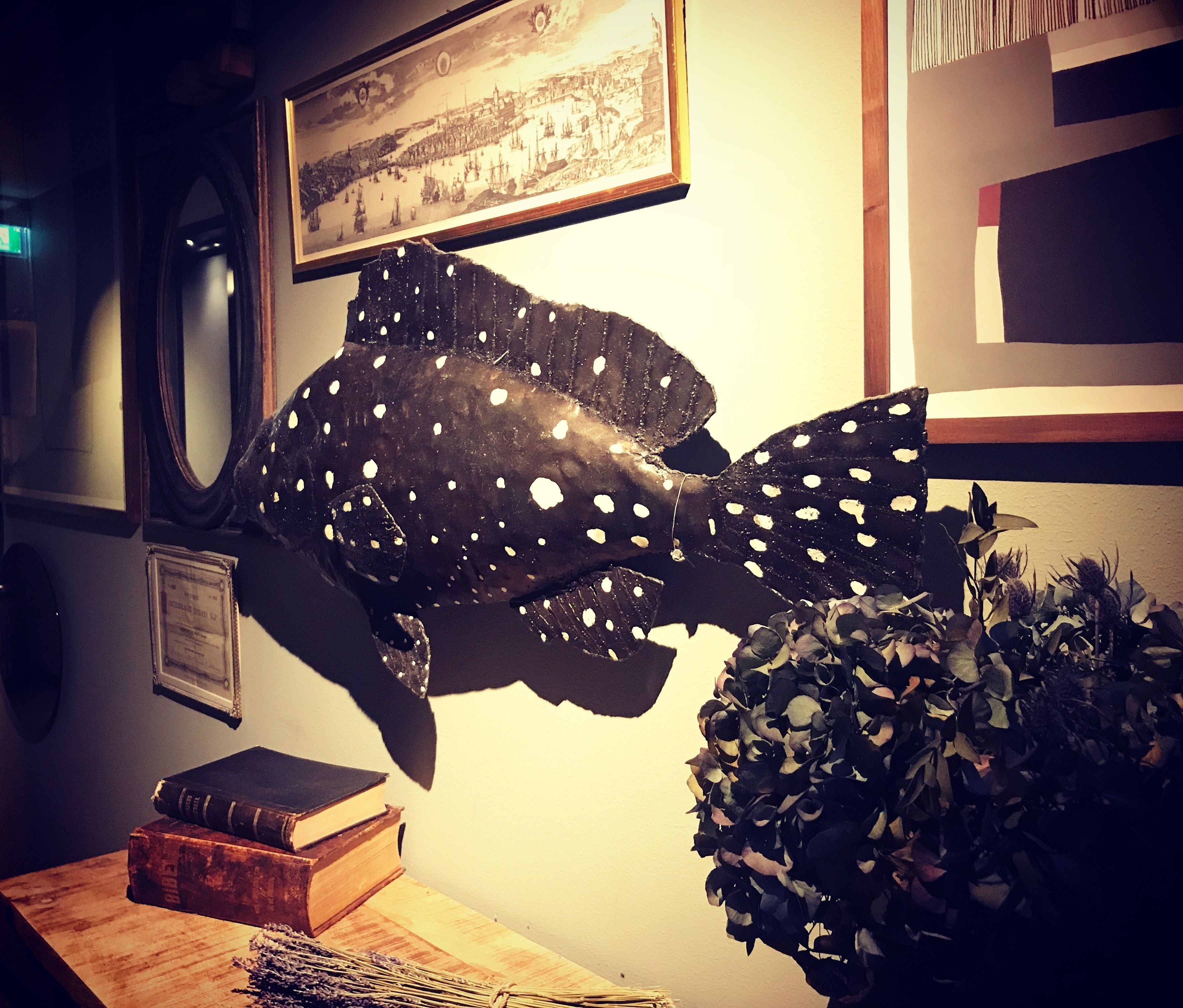 A room with a large fish decoration, a framed picture on the wall, and a plant on the table.