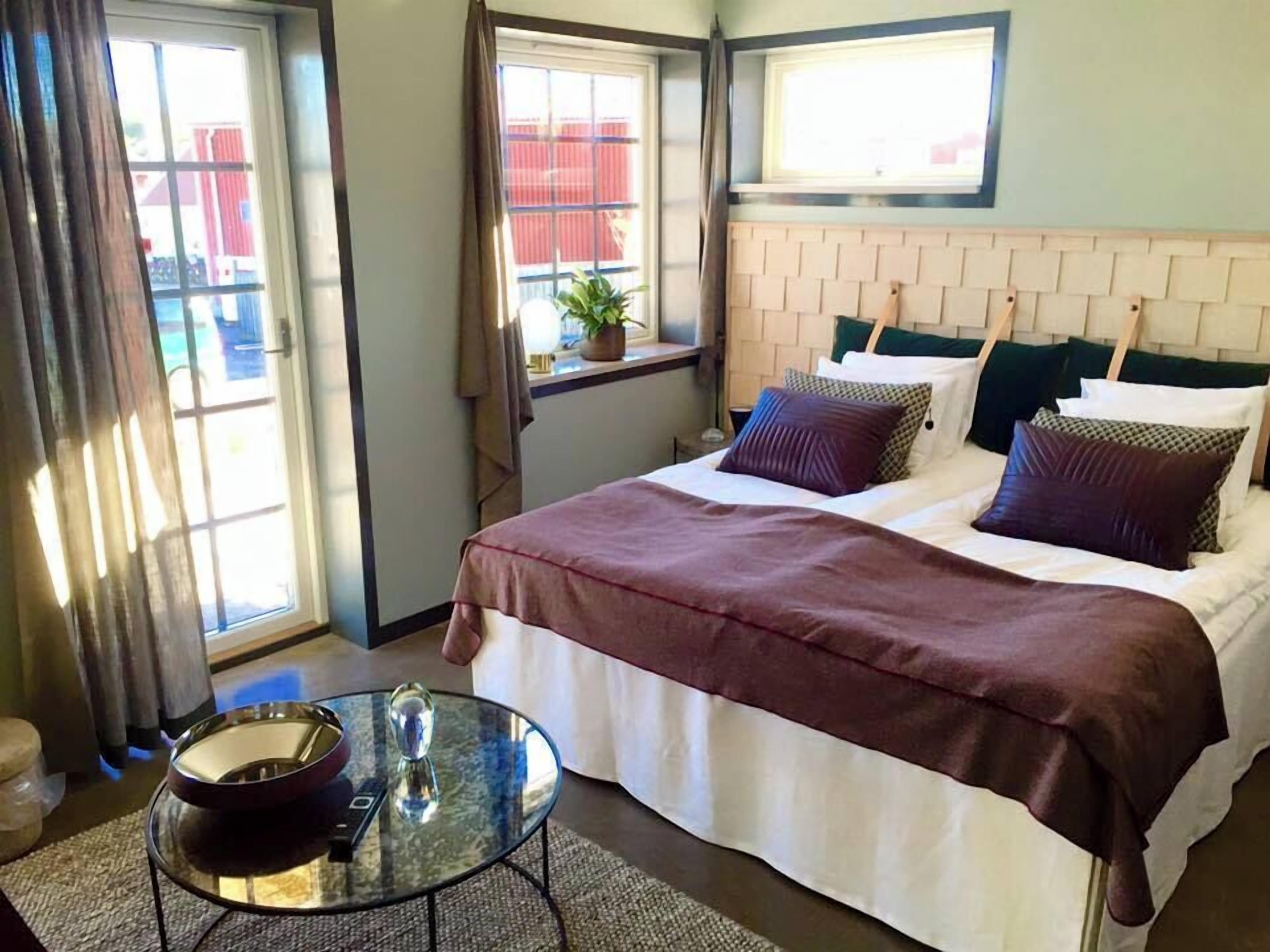 A hotel room with a bed, a small table with a bowl and a glass, and a window with curtains.