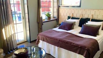 A hotel room with a bed, a small table with a bowl and a glass, and a window with curtains.
