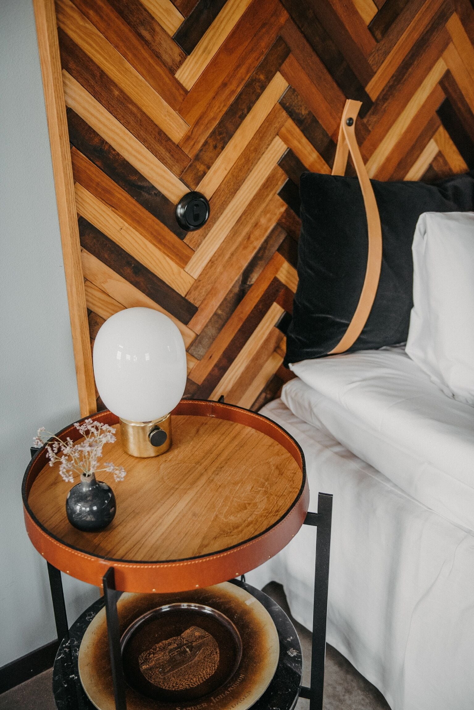 Habitación con pared de madera en patrón de espiga, una mesa redonda de madera con una lámpara, un cuenco pequeño y una silla negra.