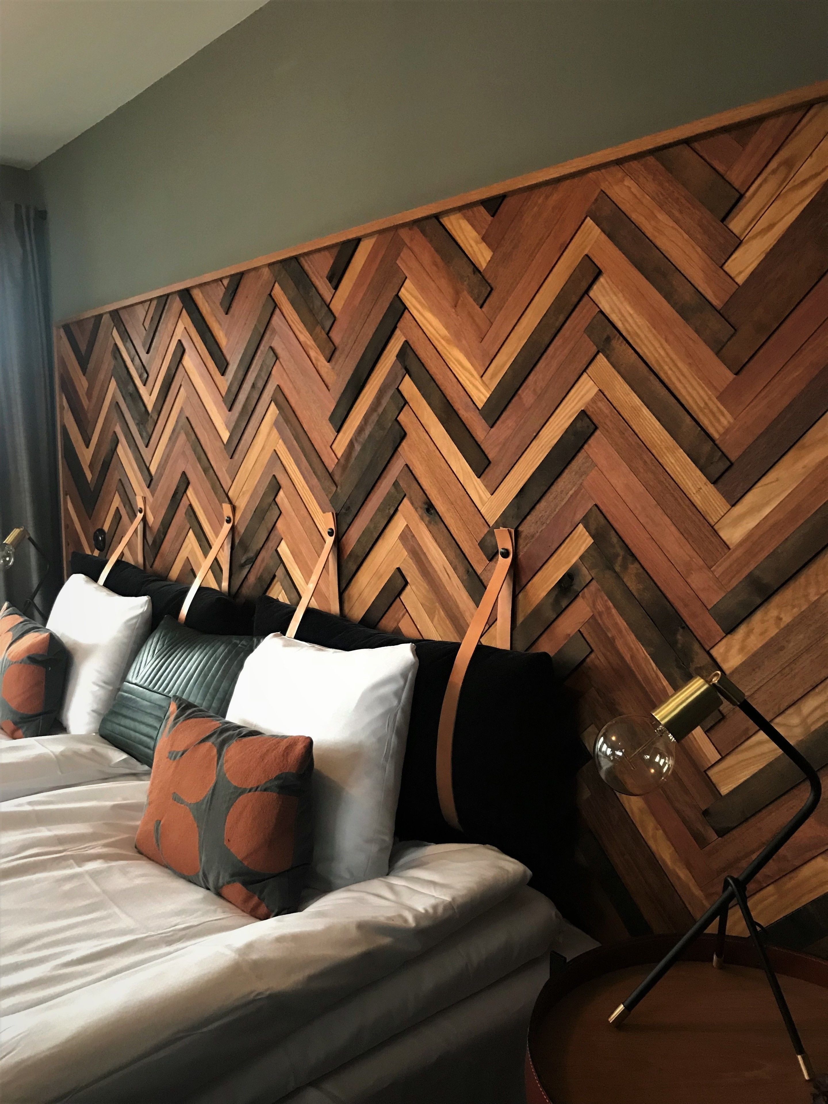 A hotel room with a bed, pillows, a lamp, and a wooden wall panel.