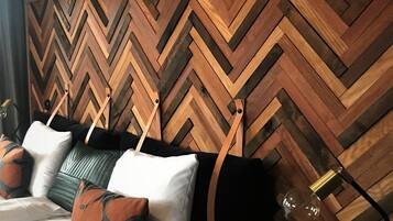 A hotel room with a bed, pillows, a lamp, and a wooden wall panel.