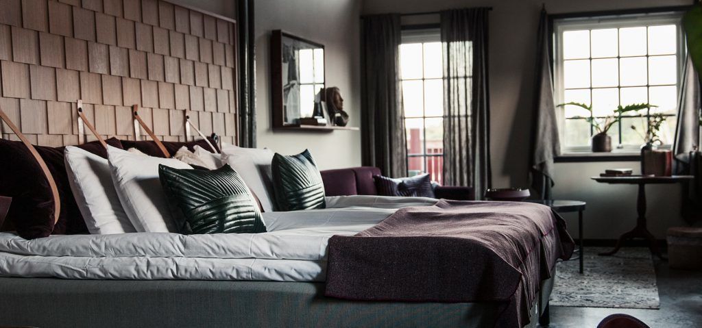 A modern bedroom with a large bed, a wooden headboard, a small table, and a window with curtains.