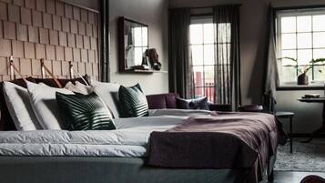 A modern bedroom with a large bed, a wooden headboard, a small table, and a window with curtains.