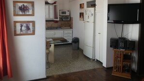 Eine kompakte Küche mit weißen Schränken, einer Mikrowelle, einem Kühlschrank und einem Fernseher auf einem Holzboden.