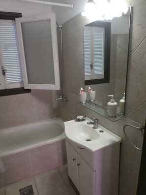 A bathroom with a bathtub, a sink, a mirror, and toiletries on the countertop. - Departamento-casa muy amplio y céntrico. (Luján)