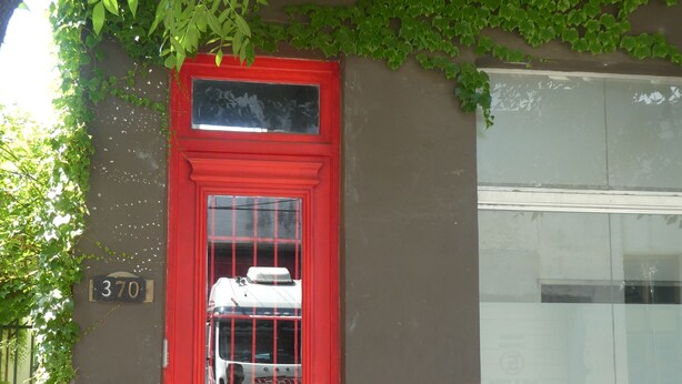 Eine rote Tür mit Fenster, einer Nummernschild und ein Gebäude mit Glasfenster.