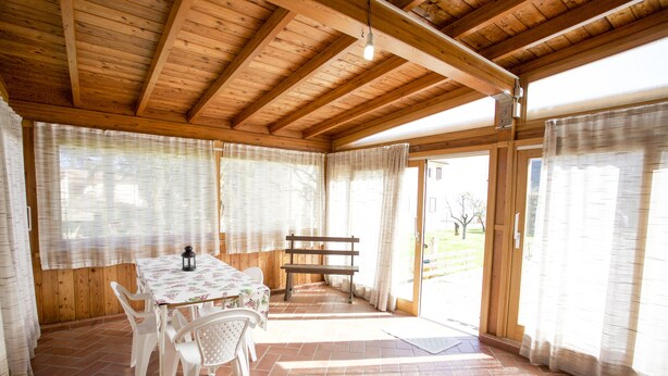 Une pièce aux murs lambrés, avec une table et des chaises, un banc et une vue sur l’extérieur à travers une porte vitrée.