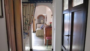 Un pasillo estrecho que conduce a un dormitorio con cama, una silla y una mesita.