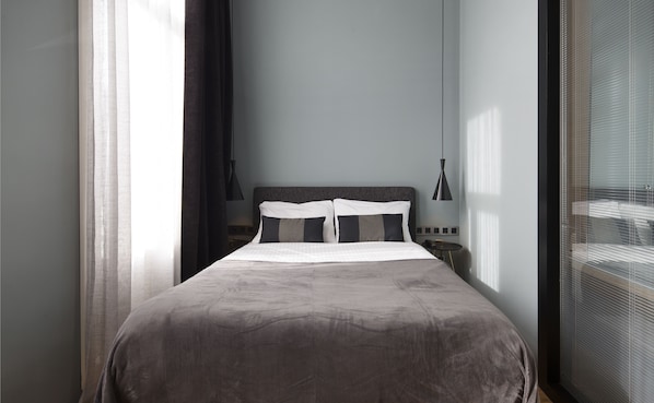 A neatly made bed with a dark brown cover, a headboard with a textured pattern, and a bedside table with a lamp. - Quentin Zoo hotel (Amsterdam)