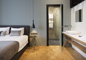 Un dormitorio moderno con cama, mesita de noche y baño con lavamanos y espejo.