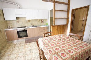 A compact kitchen with a dining area, featuring a tiled floor, wooden cabinets, a stove, and a table with a floral tablecloth.