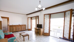 A spacious living room with a stone floor, a wooden cabinet, a television, and a balcony with a view. - Appartamento Quadri Azzurro (Porto Azzurro)