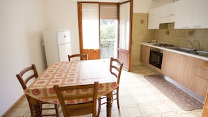 A small kitchen with a dining table, chairs, a refrigerator, a stove, and cabinets. - Appartamento Quadri Azzurro (Porto Azzurro)