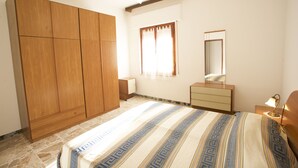 A bedroom with a large wardrobe, a bed with a patterned bedspread, a bedside table with a lamp, and a mirror on the wall. - Appartamento Quadri Azzurro (Porto Azzurro)