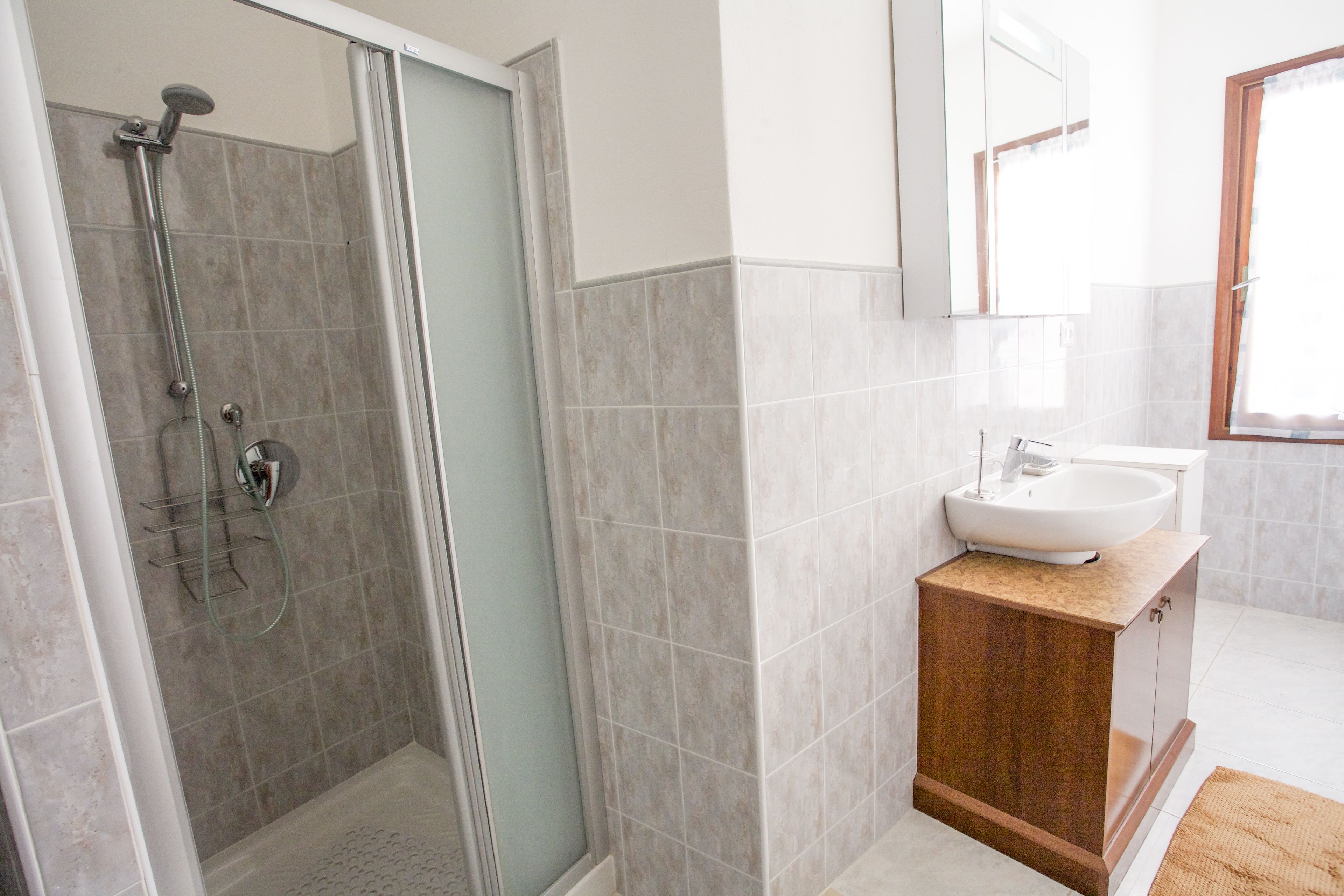 Un baño moderno con ducha envuelta en vidrio, tocador de madera con lavamanos y un espejo grande sobre el tocador.