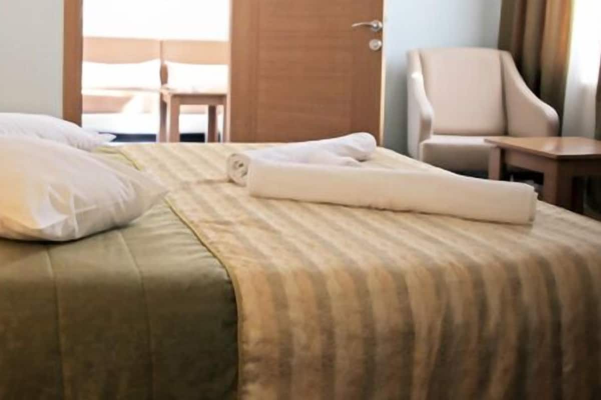 A neatly made bed with pillows and a rolled towel, a chair, and a lamp in a hotel room.