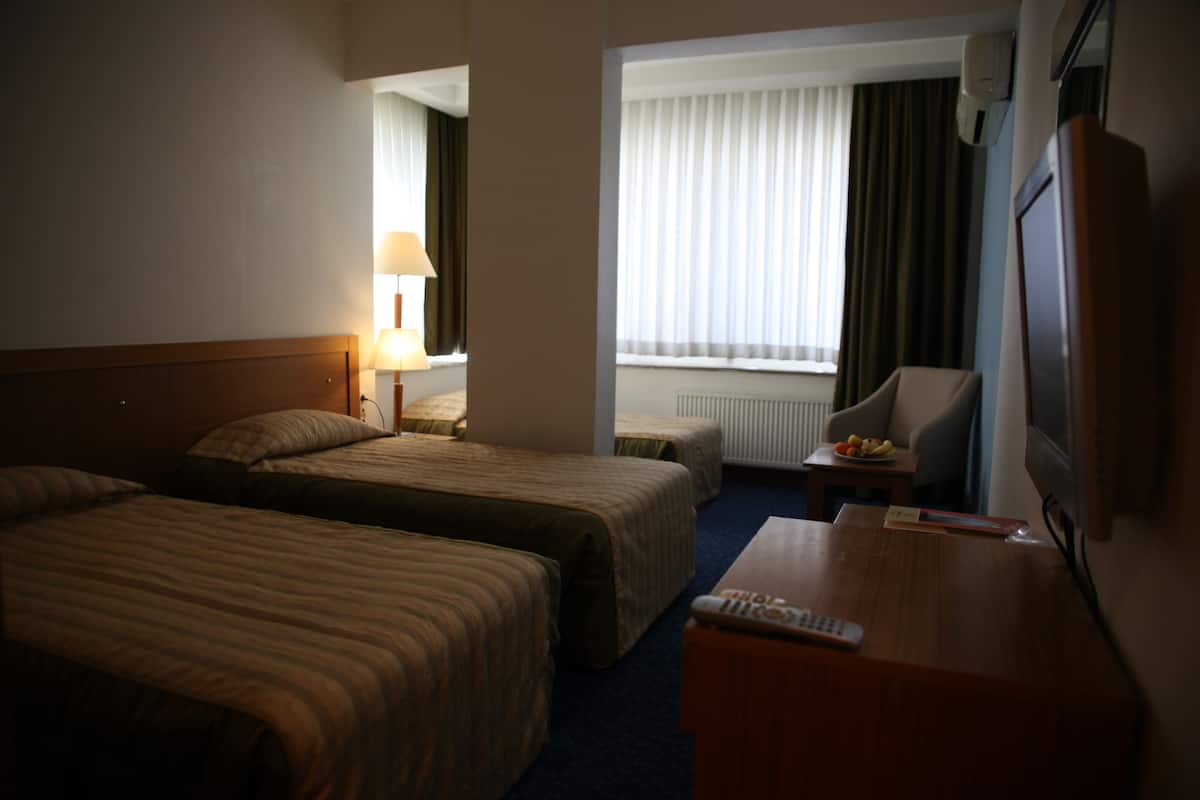 A hotel room with two beds, a desk, a chair, a lamp, and a window with curtains.