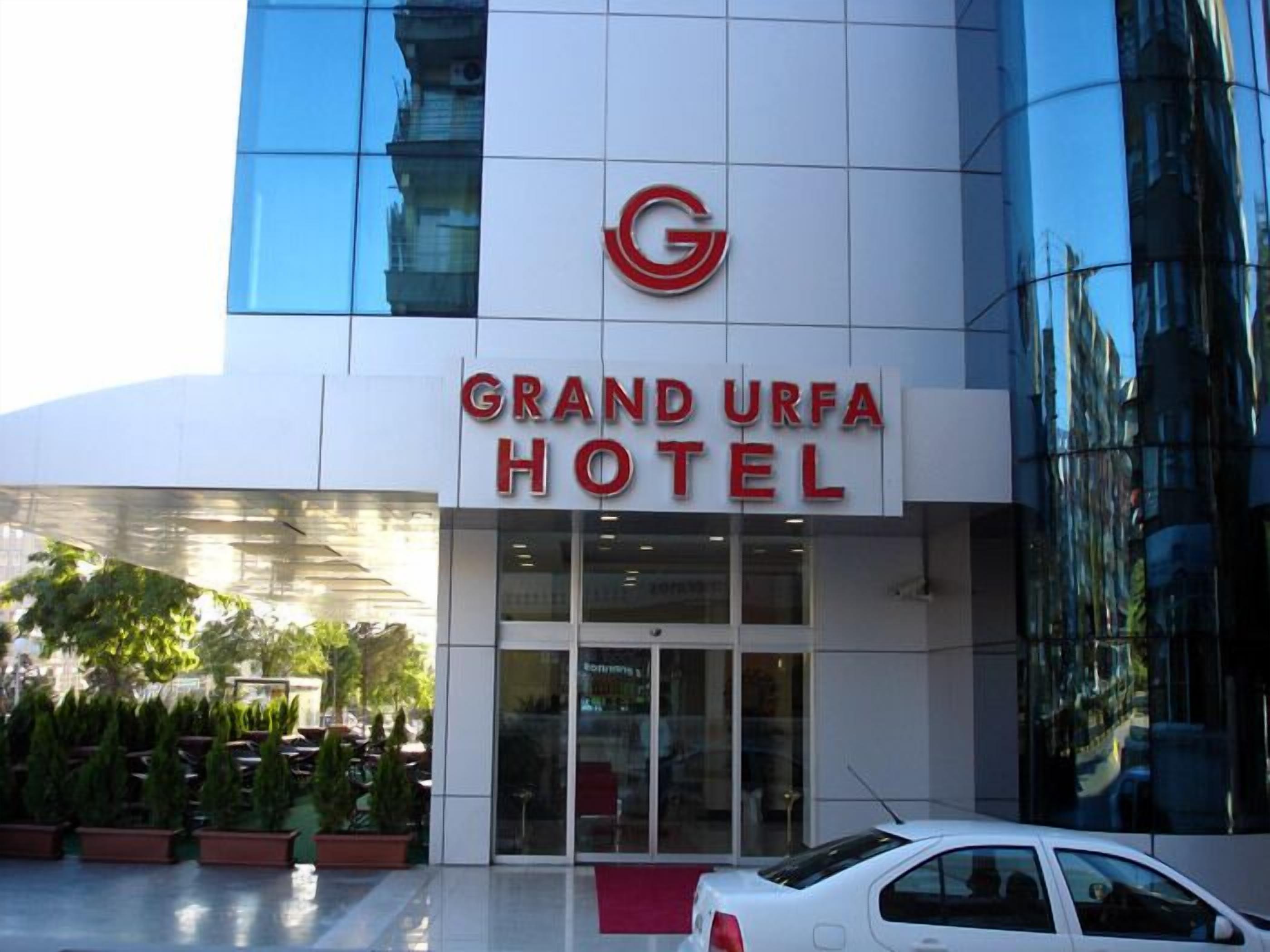 The exterior of the Grand Urfa Hotel with a modern glass facade and a prominent red logo.