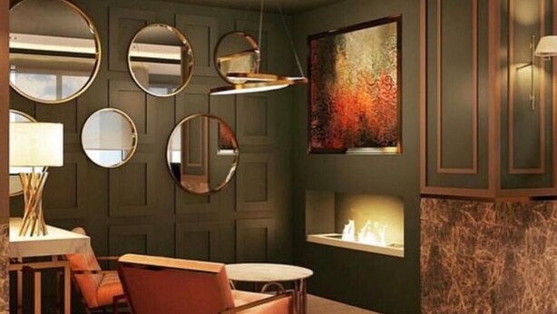 A room with a dining area featuring a table and chairs, multiple round mirrors on the wall, a fireplace with a marble surround, and a large abstract painting above the fireplace. - Grand Urfa Hotel (Sanliurfa)