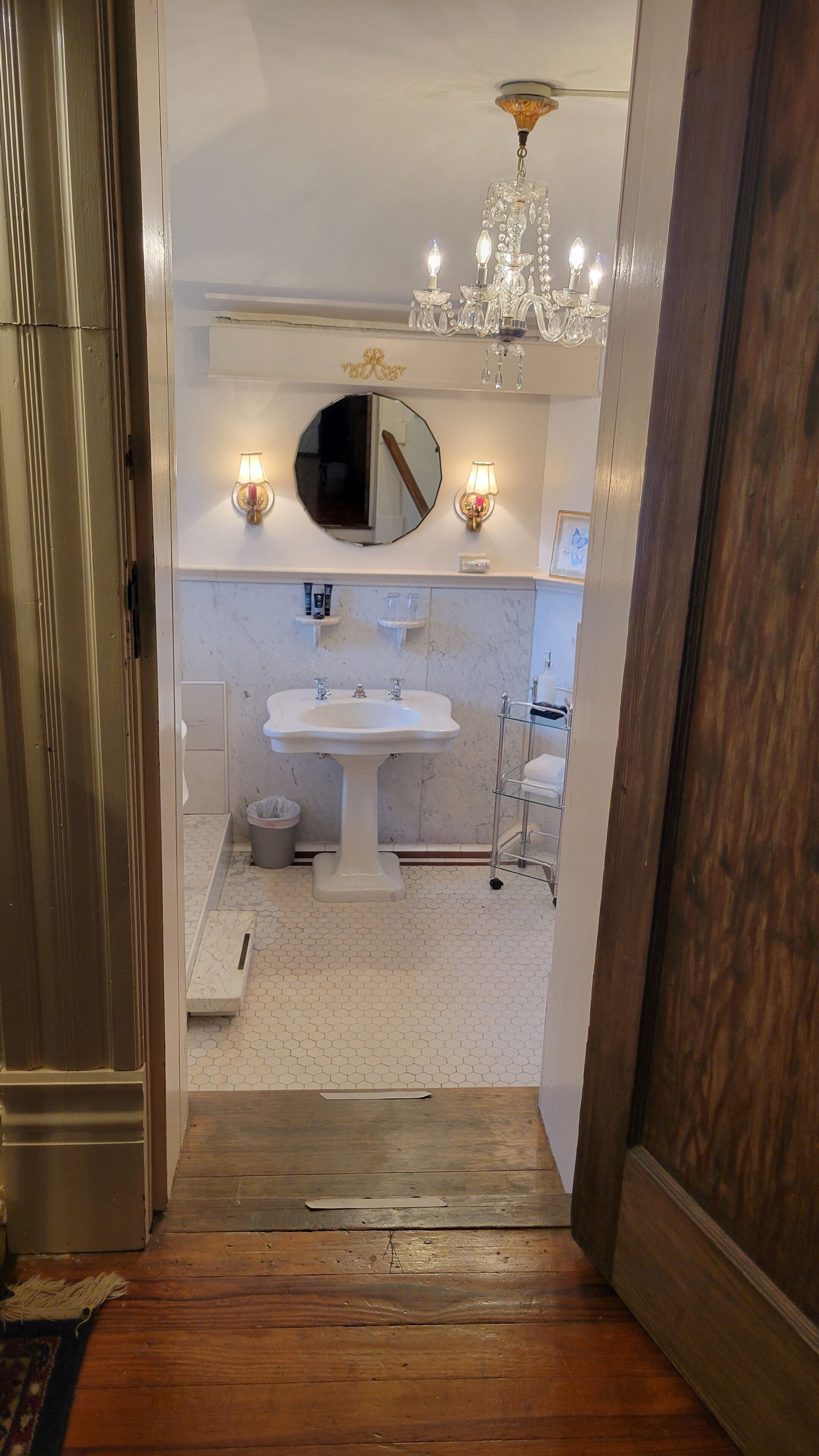 A bathroom with a pedestal sink, a round mirror, and a chandelier.