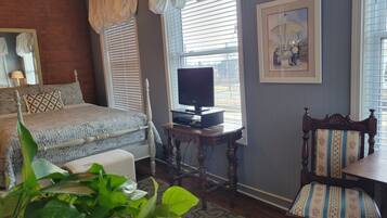 A bedroom with a bed, a television on a stand, a chair, and a window with blinds.