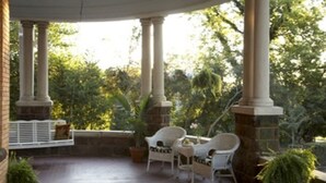 A covered patio with white wicker chairs and a stone fireplace. - 1890 Williams House Inn (Hot Springs)