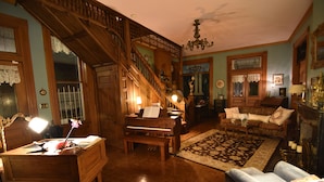 A spacious living room with a grand staircase, a piano, a sofa, and a coffee table. - 1890 Williams House Inn (Hot Springs)