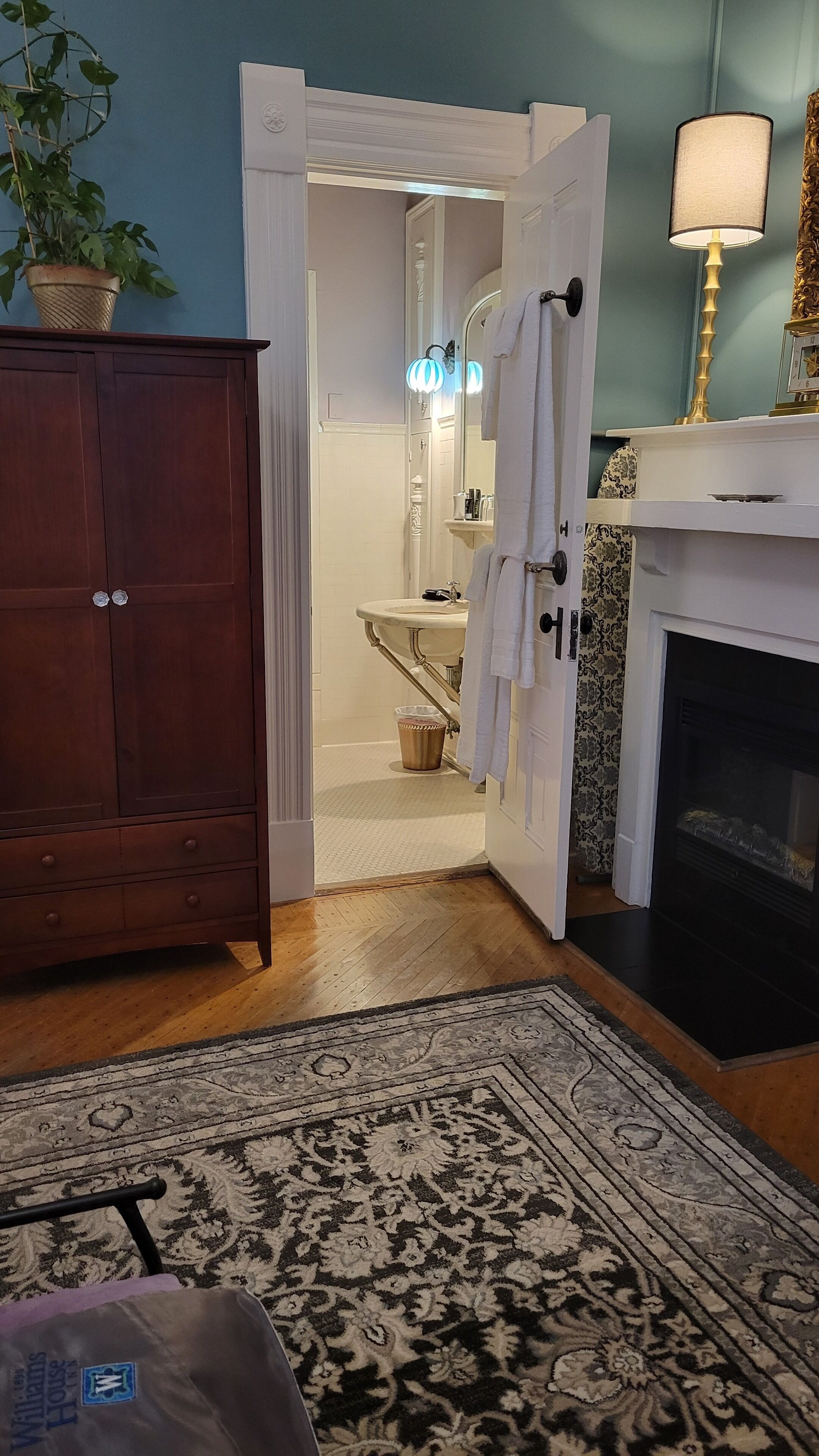 A room with a wooden cabinet, a patterned rug, a white door leading to a bathroom, and a fireplace.
