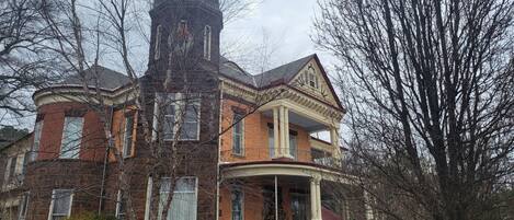 A large, historic brick building with a prominent tower, a covered porch, and a symmetrical facade.