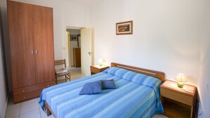 A bedroom with a bed, a wooden wardrobe, a nightstand with a lamp, and a framed picture on the wall. - Appartamenti Il Marino (Marciana)