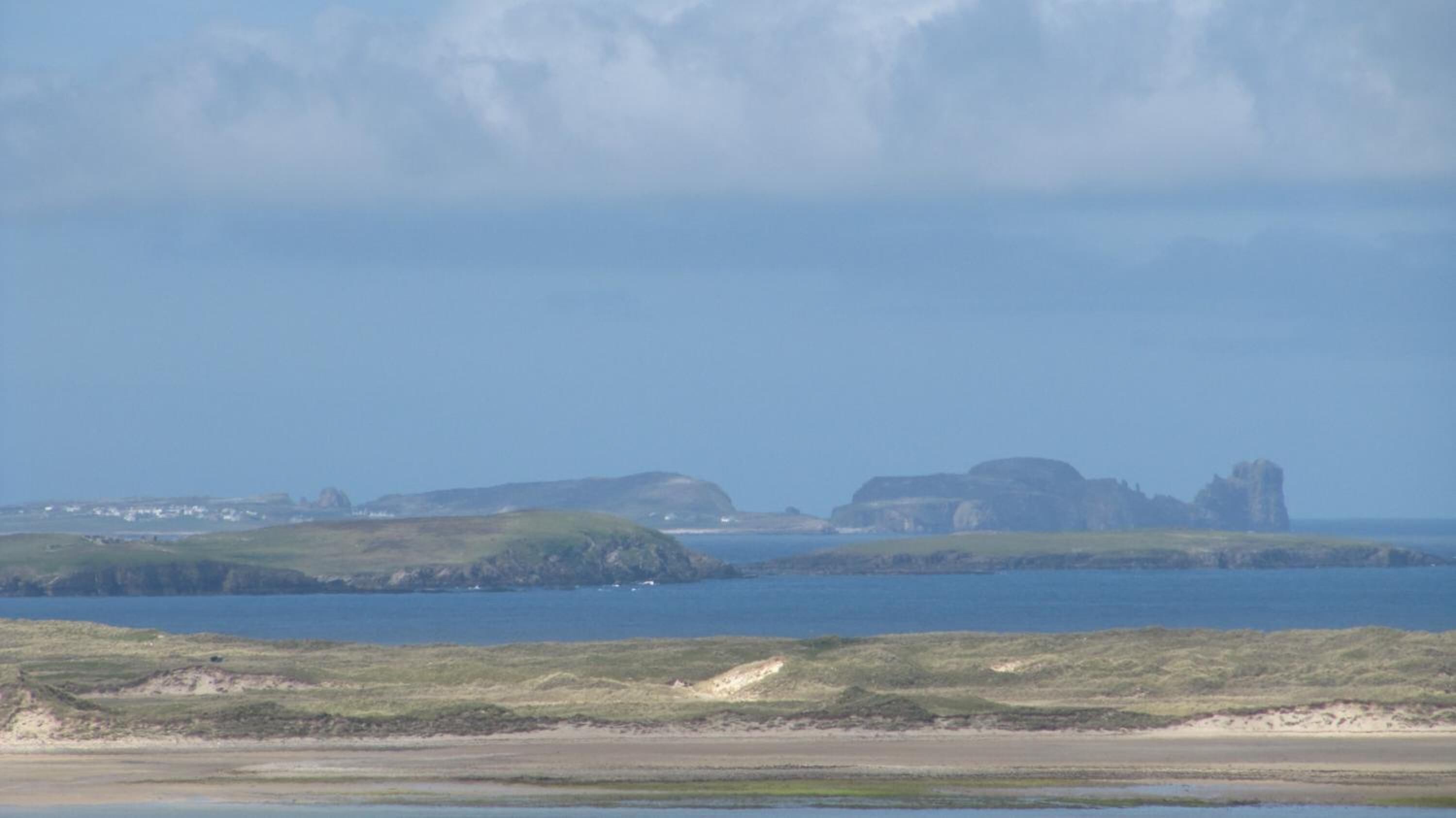 A coastal landscape with grassy areas, a body of water, and distant rocky formations.