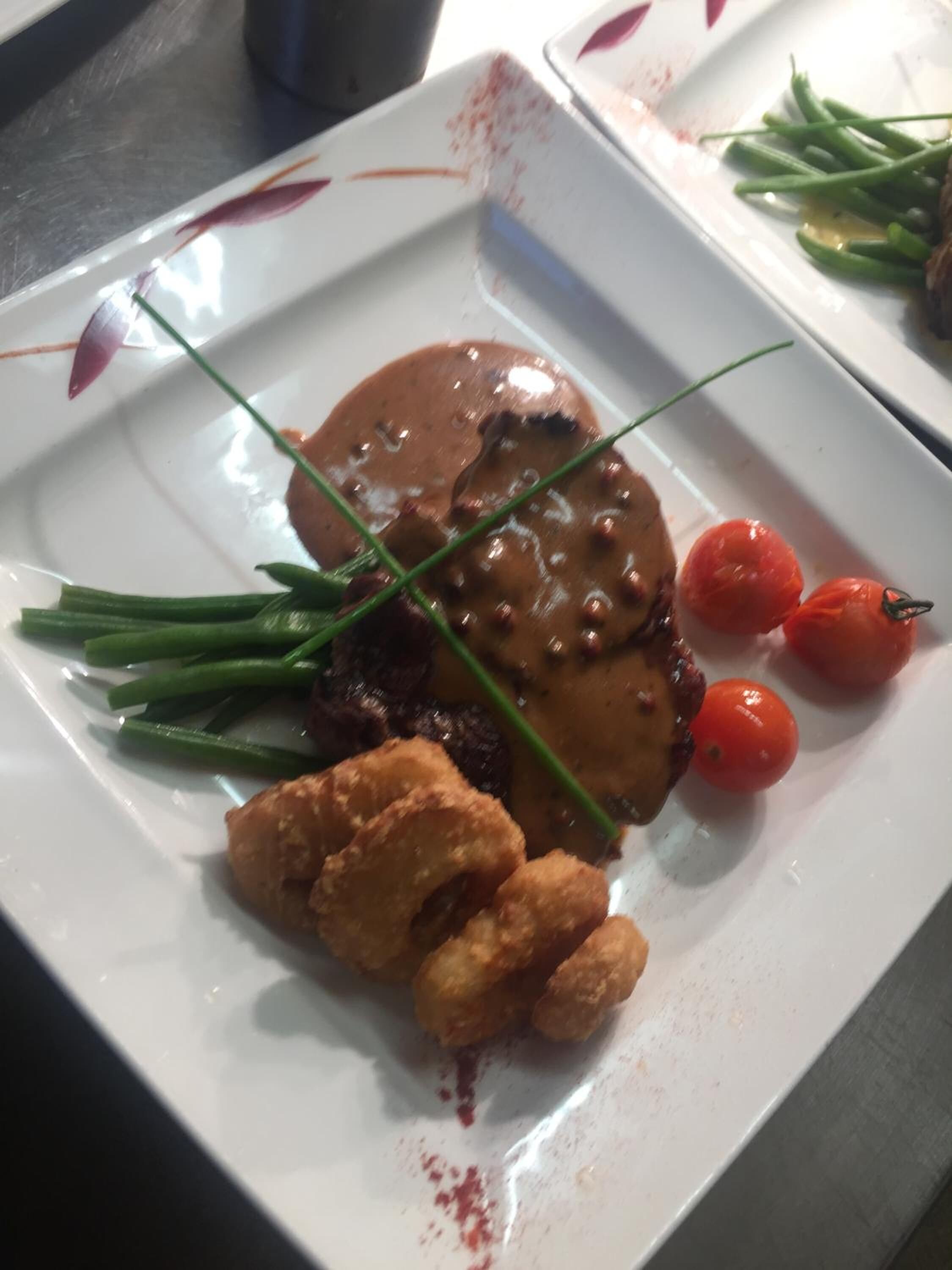 A plate with a steak, green beans, cherry tomatoes, and fried items.