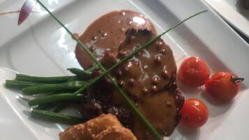 A plate with a steak, green beans, cherry tomatoes, and fried items.
