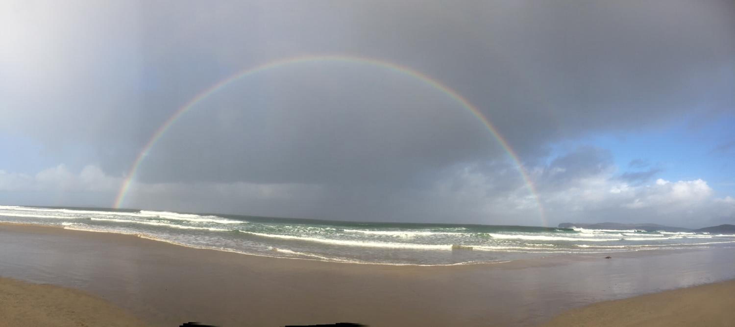 A beach with a rainbow over the ocean.