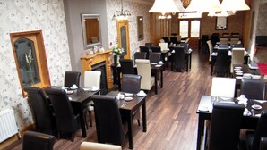 A hotel dining area with multiple tables and chairs, a fireplace, and a mirror on the wall.