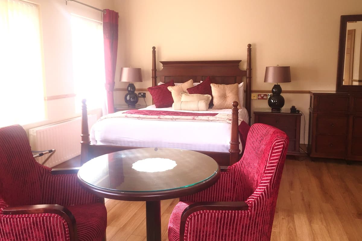 A hotel room with a wooden bed, two bedside lamps, a round glass table, and striped red chairs.