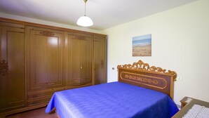 A bedroom with a large wardrobe, a bed with a blue bedspread, and a ceiling light. - Appartamento Il Marino II (Marciana)