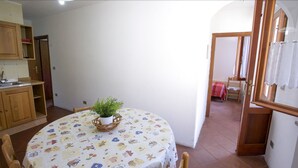 A dining area with a round table covered in a tablecloth with a pattern, surrounded by wooden chairs. A potted plant is placed in the center of the table. - Appartamento Il Marino II (Marciana)