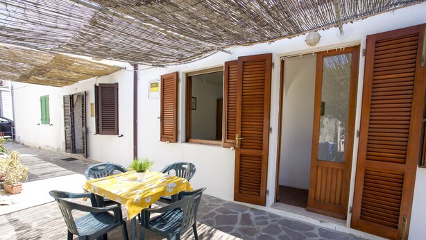 An outdoor patio with a table and chairs, wooden shutters, and a sign on the wall. - Appartamento Il Marino II (Marciana)