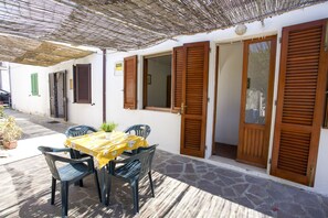 Un patio al aire libre con una mesa, sillas, contraventanas de madera y un cartel en la pared.