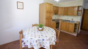 A kitchen with wooden cabinets, a dining table with a floral tablecloth, and a hanging light fixture. - Appartamento Il Marino II (Marciana)