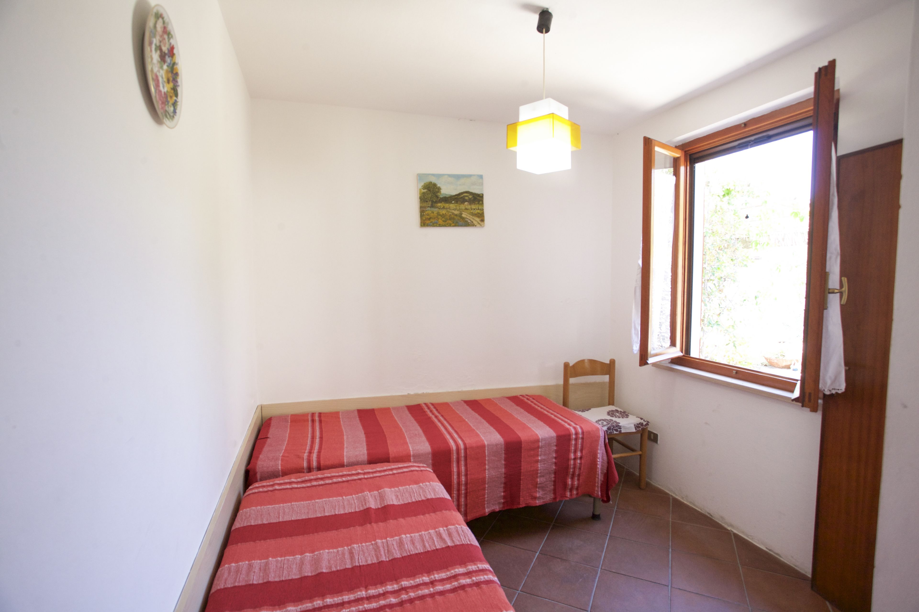 A room with two beds, a small table, a chair, a window, and a painting on the wall.
