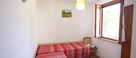 A room with two beds, a small table, a chair, a window, and a painting on the wall.