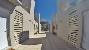 Ein schmaler, mit Fliesen ausgelegter Gang mit geschlossenen Türen an beiden Seiten, der zu einem Gebäude im modernen Baustil führt.