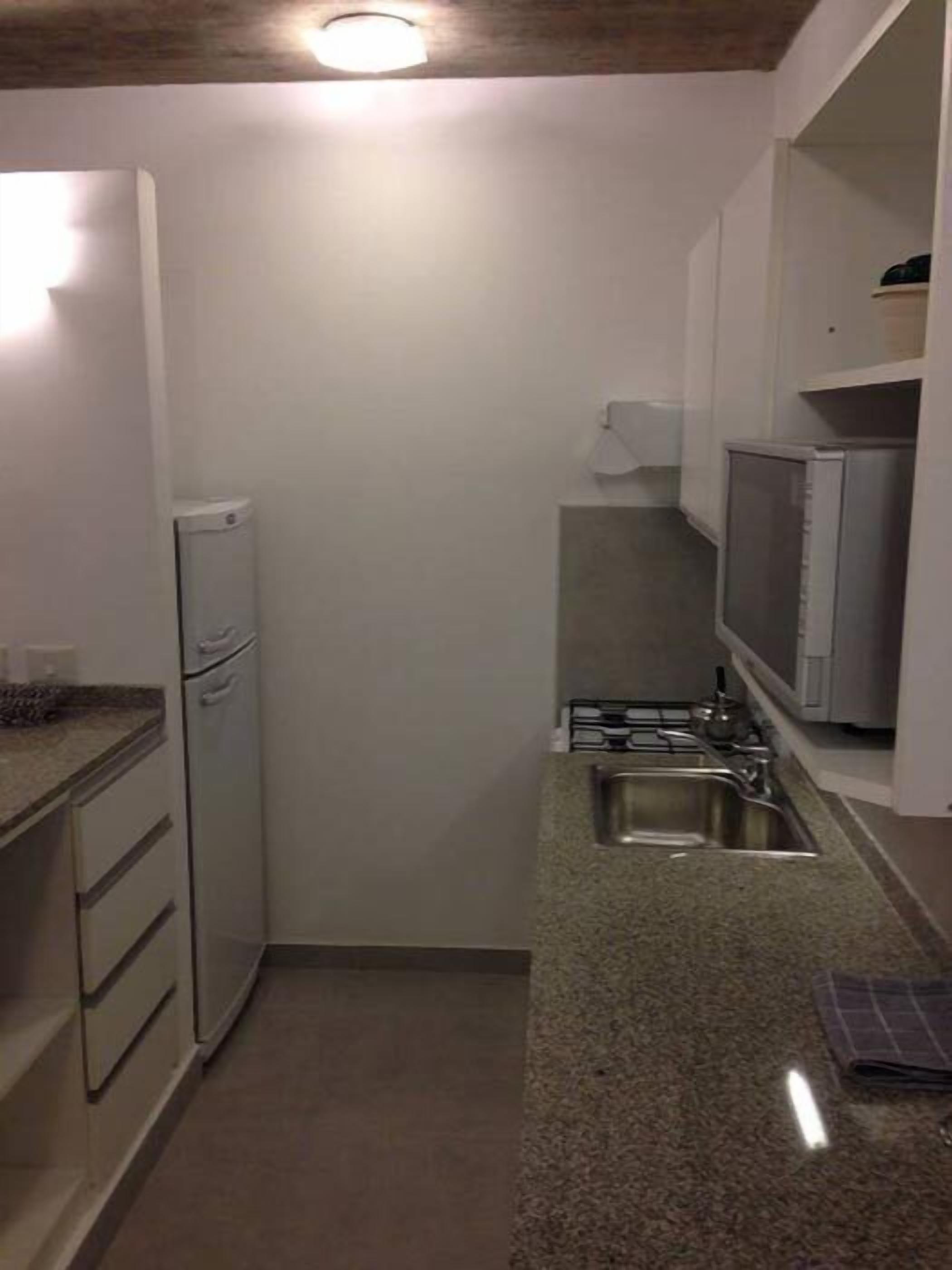 A compact kitchen with a refrigerator, microwave, sink, and granite countertop.