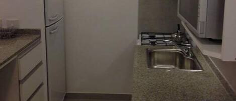 A compact kitchen with a refrigerator, microwave, sink, and granite countertop.