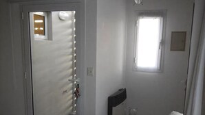 Ein Zimmer mit einer Schiebetür zu einem Badezimmer, einem kleinen Fenster und einem Sofa mit Kissenstreifen.